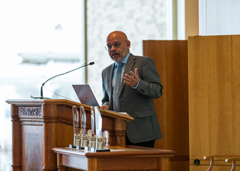 Man speaking at a podium with his hand outstretched